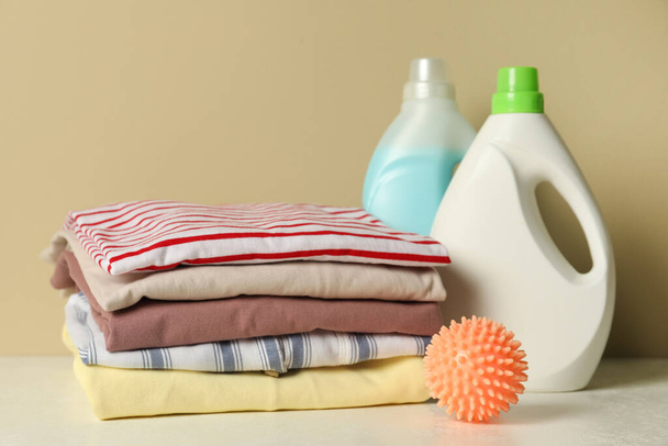Orange dryer ball, laundry detergents and stacked clean clothes on white table - Фото, зображення