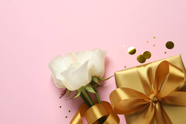 Beautiful golden gift box, flowers and confetti on pink background, flat lay. Space for text - Foto, immagini