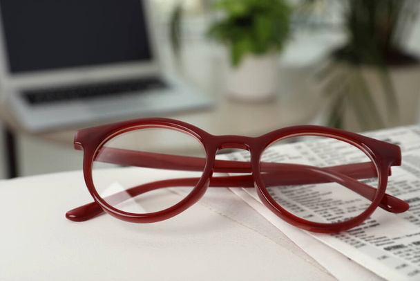 Glasses and newspaper on armrest indoors, closeup - Photo, image