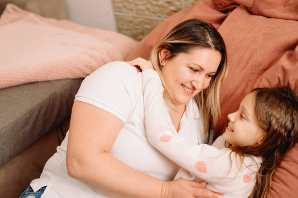 Fille et mère allongées sur un grand oreiller s'embrassant avec une expression faciale souriante, du temps en famille ensemble. - Photo, image