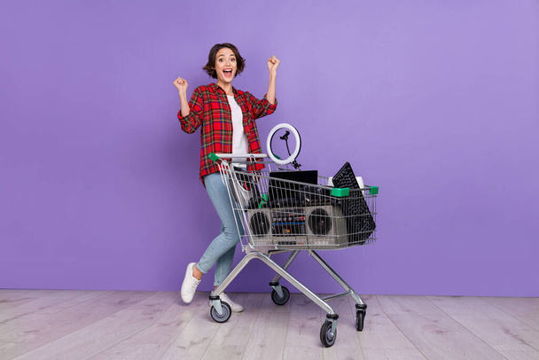 Full size photo of nice millennial brunette lady with resale trolley wear shirt jeans footwear isolated concrete violet wall background - 写真・画像