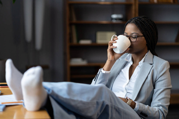 Afro woman freelancer relaxing at remote workplace with cup of tea. Benefits of working from home - Foto, Bild