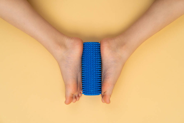 rodillo de aguja azul para masaje y fisioterapia sobre fondo beige con la imagen de un pie de niño, el concepto de prevención y tratamiento del hallux valgus - Foto, Imagen