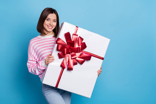 Photo of cute young brunette lady hold large present wear pink jumper isolated on blue background - Zdjęcie, obraz