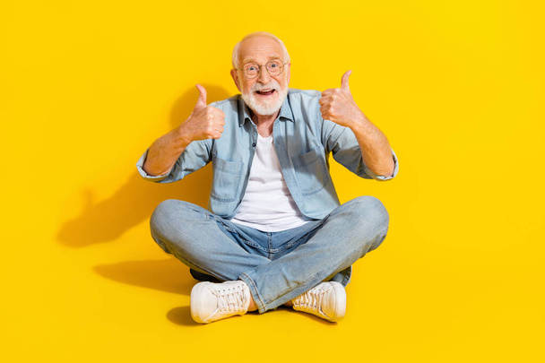 Πορτρέτο του ελκυστική χαρούμενη γκρίζα μαλλιά άνθρωπος κάθεται θέση λωτού δείχνει μικρογραφία απομονώνονται σε φωτεινό κίτρινο χρώμα φόντο - Φωτογραφία, εικόνα