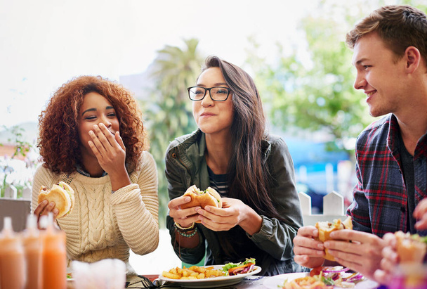 Gutes Essen und Lachen gehen Hand in Hand. Schnappschuss von drei Freunden, die im Freien Burger essen. - Foto, Bild