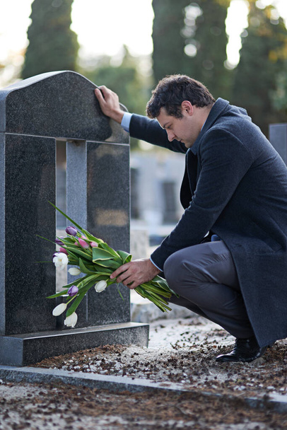 Sie waren ihre Lieblingsblumen. Aufnahme eines jungen Mannes, der einen Friedhof mit einem Blumenstrauß besucht. - Foto, Bild