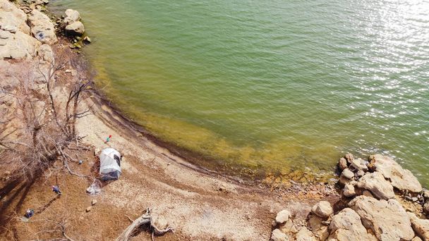 Aerial view row of fishing poles near large family tent along rocky shoreline and sandstone cliff at Grapevine Lake, Texas, America. Camping, actividades recreativas en invierno - Foto, Imagen
