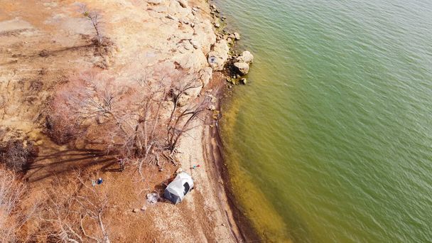 Antenninäköala rivi kalastus pylväät lähellä suuri perhe teltta pitkin kivinen rantaviiva ja hiekkakivi kallio Grapevine Lake, Texas, Amerikka. Telttailu, virkistystoiminta talvella - Valokuva, kuva