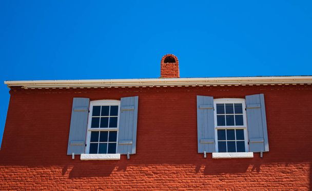 古い家の外壁に孤独な窓。2つの窓と古い赤い壁の灰。ストリートビュー、旅行写真、選択的フォーカス - 写真・画像