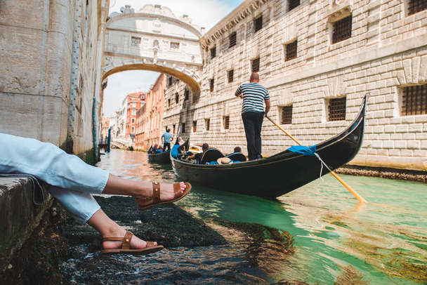 ゴンドラのコピースペースで運河の眺めを楽しむヴェネツィアイタリアの都市岸壁に座っている女性 - 写真・画像