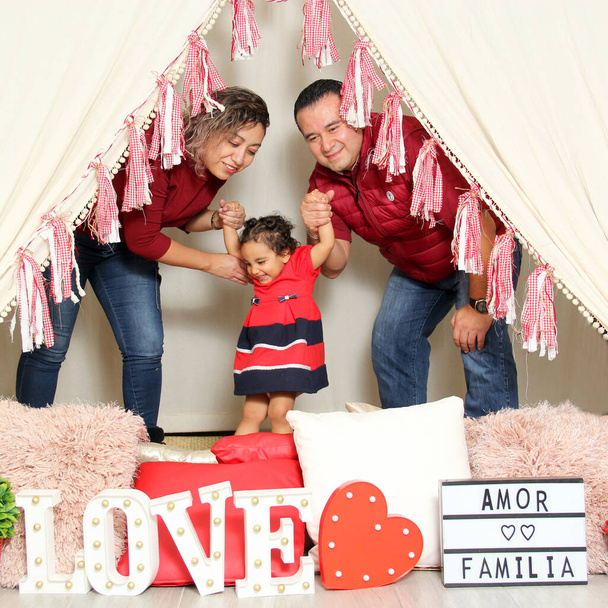 Latina mom, dad and daughter show their affection under a teepee with a sign that says "Love and family" celebrate Valentine's Day of Love and Friendship in February - Photo, Image