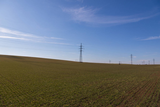 Nagyfeszültségű oszlopok villamosenergia-elosztás a vidéken. A háttérben egy kék ég, drámai felhőkkel.. - Fotó, kép