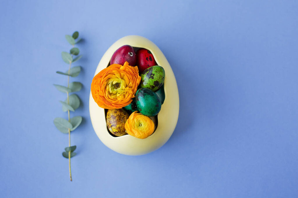 Easter eggs and orange flowers in the yellow bowl on a blue background. Easter colorful concept - Fotografie, Obrázek