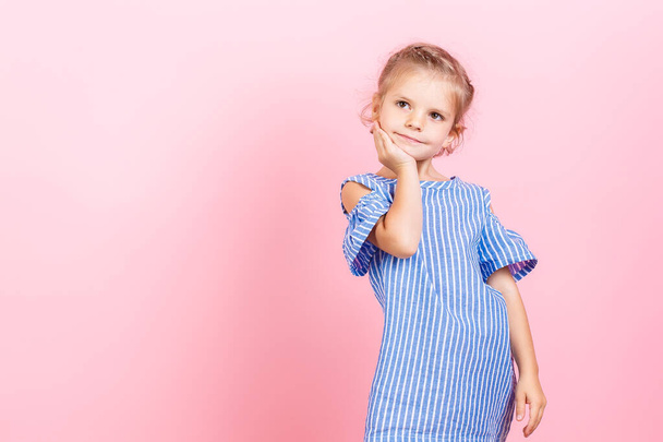Portrait of cute little child girl wears blue dress while posing over pink studio background - Photo, Image