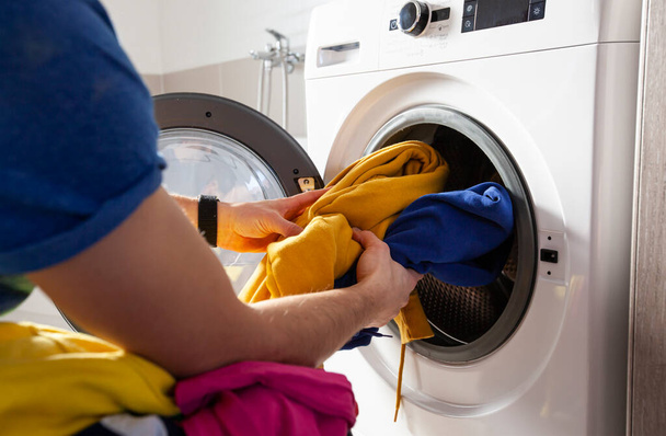 Man loading the washer dryer with clothes  - Foto, Imagen
