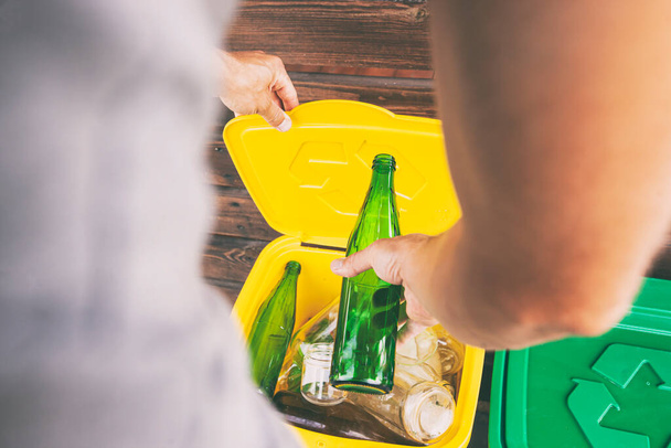 Man throwing the glass bottle into one of three dustbins for sorting trash - Fotoğraf, Görsel