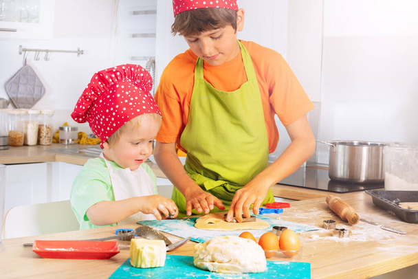 Two happy boy brothers cut out forms from dough at kitchen cooking cookies at home - Φωτογραφία, εικόνα