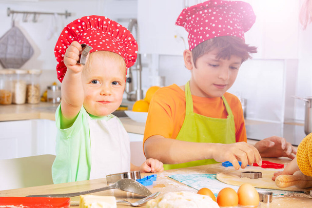 Little toddler and brother roll dough cut out cookies on the kitchen wearing chef hats - Foto, immagini