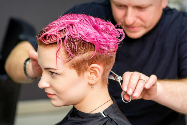 Egy nőnek új frizurája van. A férfi fodrász vágja festett rózsaszín rövid haj ollóval egy fodrászszalonban - Fotó, kép