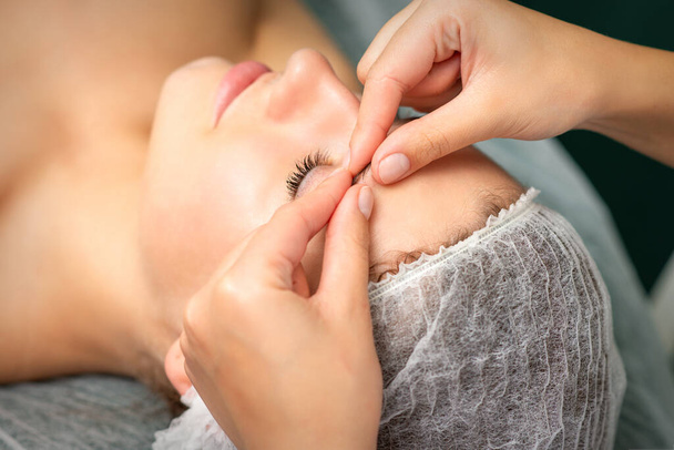 Massage manuel du visage sculptant dans le spa. Doigts de l'esthéticienne faire des sourcils de massage facial d'une jeune femme en clinique de cosmétologie, gros plan - Photo, image
