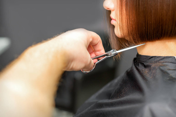 Una mujer con un nuevo corte de pelo. Peluquero masculino que corta el cabello castaño con tijeras en una peluquería - Foto, imagen
