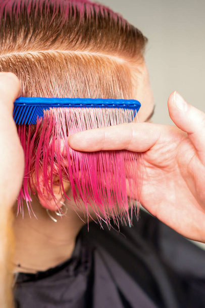 Mains de coiffeur peignage cheveux faisant coiffure rose courte pour une jeune femme caucasienne dans un salon de beauté - Photo, image