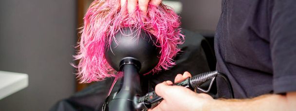 Estilista haciendo peinado usando secador de pelo soplando en mojado pelo rosa personalizado en un salón de belleza - Foto, imagen