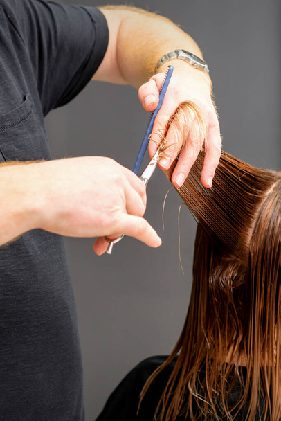 Una mujer con un nuevo corte de pelo. Peluquero masculino que corta el cabello castaño con tijeras en una peluquería - Foto, Imagen