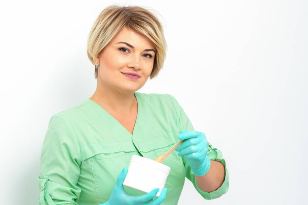 Cosmetician holding a jar of wax for depilation smiling on a white background. Natural product for hair removal. Copy space - Fotoğraf, Görsel