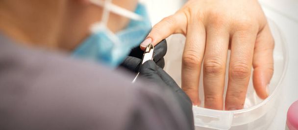 Nagelmeester verwijdert nagels nagelriemen met een tepel, manicure hygiëne in een schoonheidssalon - Foto, afbeelding