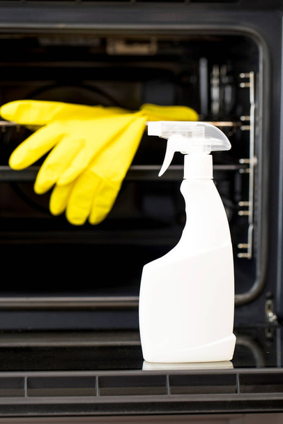 On the door of an open oven is a mock-up of a white spray bottle with oven detergent. General cleaning of the kitchen. - Фото, изображение