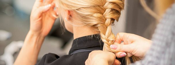 Плетіння коси. Руки жіночої перукарні довга коса для блондинки в перукарні
 - Фото, зображення