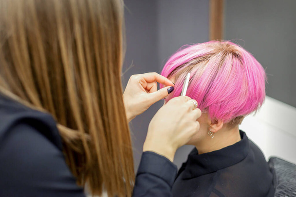 Cabeleireiro prepara tingido cabelo rosa curto de uma jovem mulher para procedimentos em um salão de beleza - Foto, Imagem