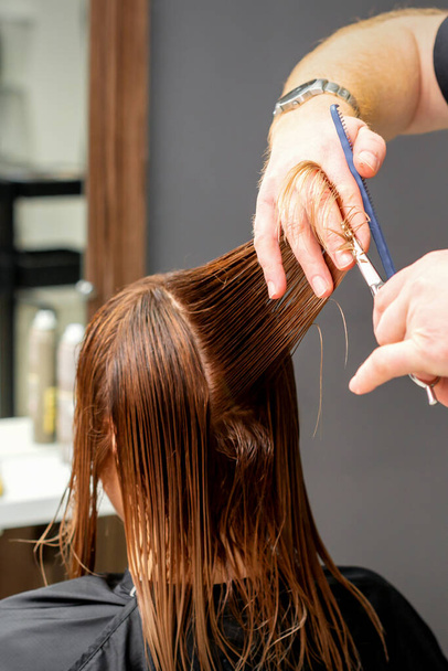 Een vrouw met een nieuw kapsel. man hairstylist knippen bruin haar met schaar in een kapsalon - Foto, afbeelding