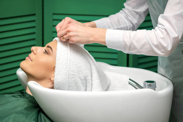Um cabeleireiro está embrulhando uma cabeça feminina em uma toalha depois de lavar o cabelo no salão de beleza - Foto, Imagem