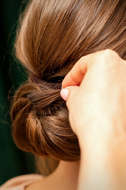 Mani di parrucchiere che fanno torcere l'acconciatura francese di una giovane donna bruna irriconoscibile in un salone di bellezza, vista posteriore, primo piano - Foto, immagini