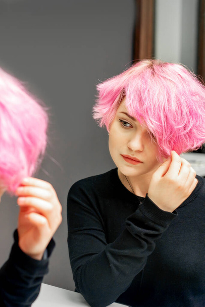 Bella giovane donna caucasica guardando i suoi capelli corti rosa in uno specchio - Foto, immagini