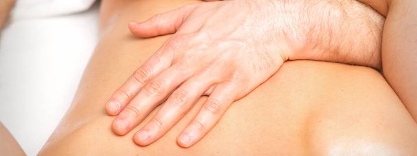 Męski fizjoterapeuta rozciąga ramiona na plecach leżącego mężczyzny, z bliska - Zdjęcie, obraz