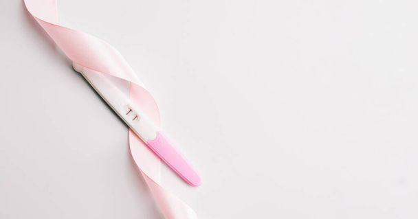 Test de grossesse isolé. Test de grossesse femme positive avec ruban de soie rose sur fond blanc. Médecine gynécologique, grossesse fertilité maternité personnes concept - Photo, image