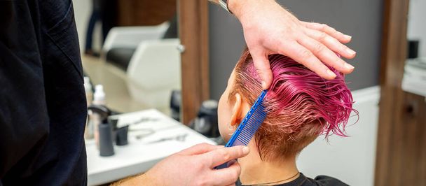 Kezek fodrász fésülködő haj, hogy rövid rózsaszín frizura egy fiatal kaukázusi nő egy szépségszalonban - Fotó, kép