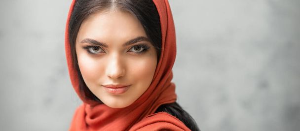 Retrato de una hermosa mujer caucásica joven con maquillaje en un pañuelo rojo sobre fondo gris - Foto, imagen