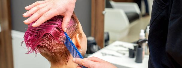 Hands of hairdresser combing hair making short pink hairstyle for a young caucasian woman in a beauty salon - Foto, Imagem