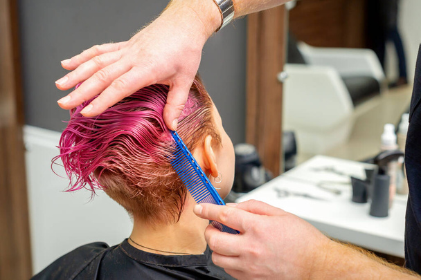 Kezek fodrász fésülködő haj, hogy rövid rózsaszín frizura egy fiatal kaukázusi nő egy szépségszalonban - Fotó, kép