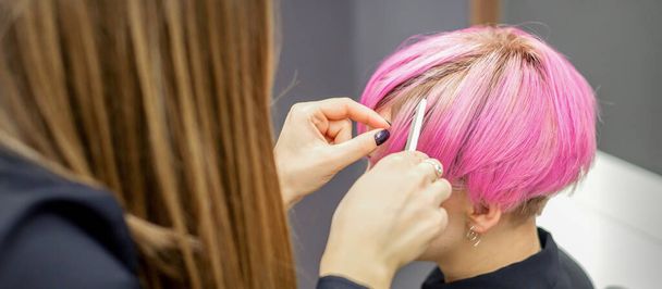 Fryzjer przygotowuje farbowane krótkie różowe włosy młodej kobiety do zabiegów w salonie piękności - Zdjęcie, obraz