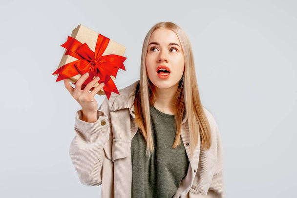 Portrait of thoughtful curious blonde girl thinking whats inside gift box, look pondering say hmm as making assumption, standing grey background - Foto, Bild