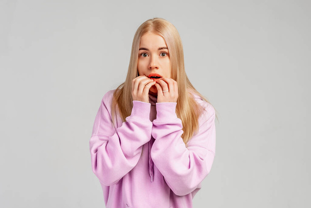 Beautiful scared young girl cover face, looks in terror at camera, shocked to hear bad news, stands against grey background. Negative human emotions concept - Photo, Image
