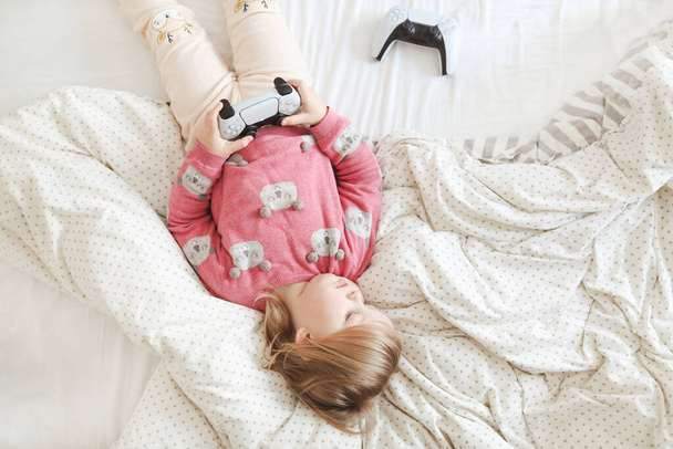 Little cute girl playing with joystick in bed at home - Foto, afbeelding