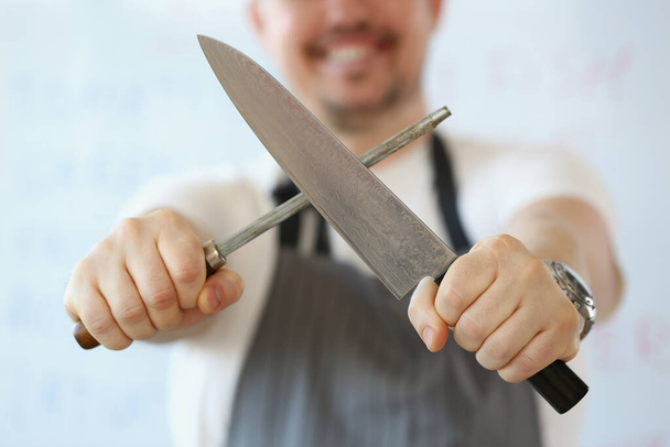 Standing man holding in hand sharp kitchenware for cooking, knife sharpening process - Photo, image