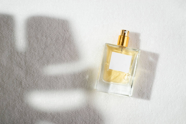 Transparante fles parfum met etiket op een witte achtergrond. Parfumpresentatie met daglicht. Trending concept in natuurlijke materialen met palmbladeren schaduw. Essentie voor vrouwen en mannen. - Foto, afbeelding